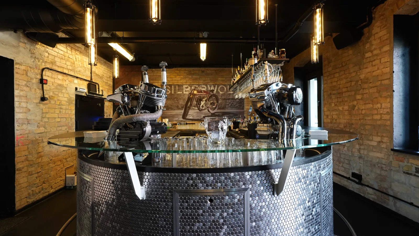 The round bar of the Silberwolf Biker Bar with two chrome engines and glasses beneath the glass top