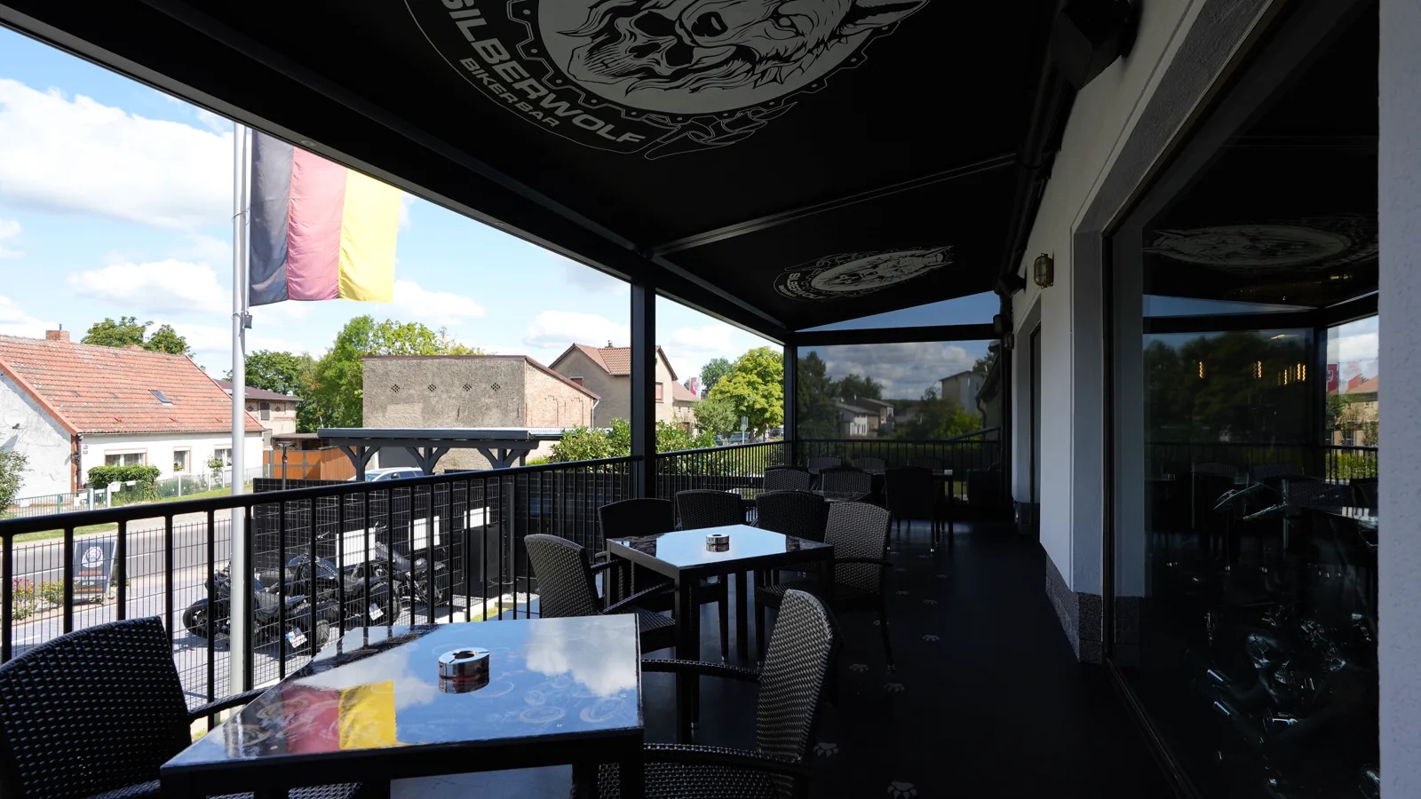 The covered terrace of the Silberwolf Biker Bar with the wolf logo on the awning and a German flag