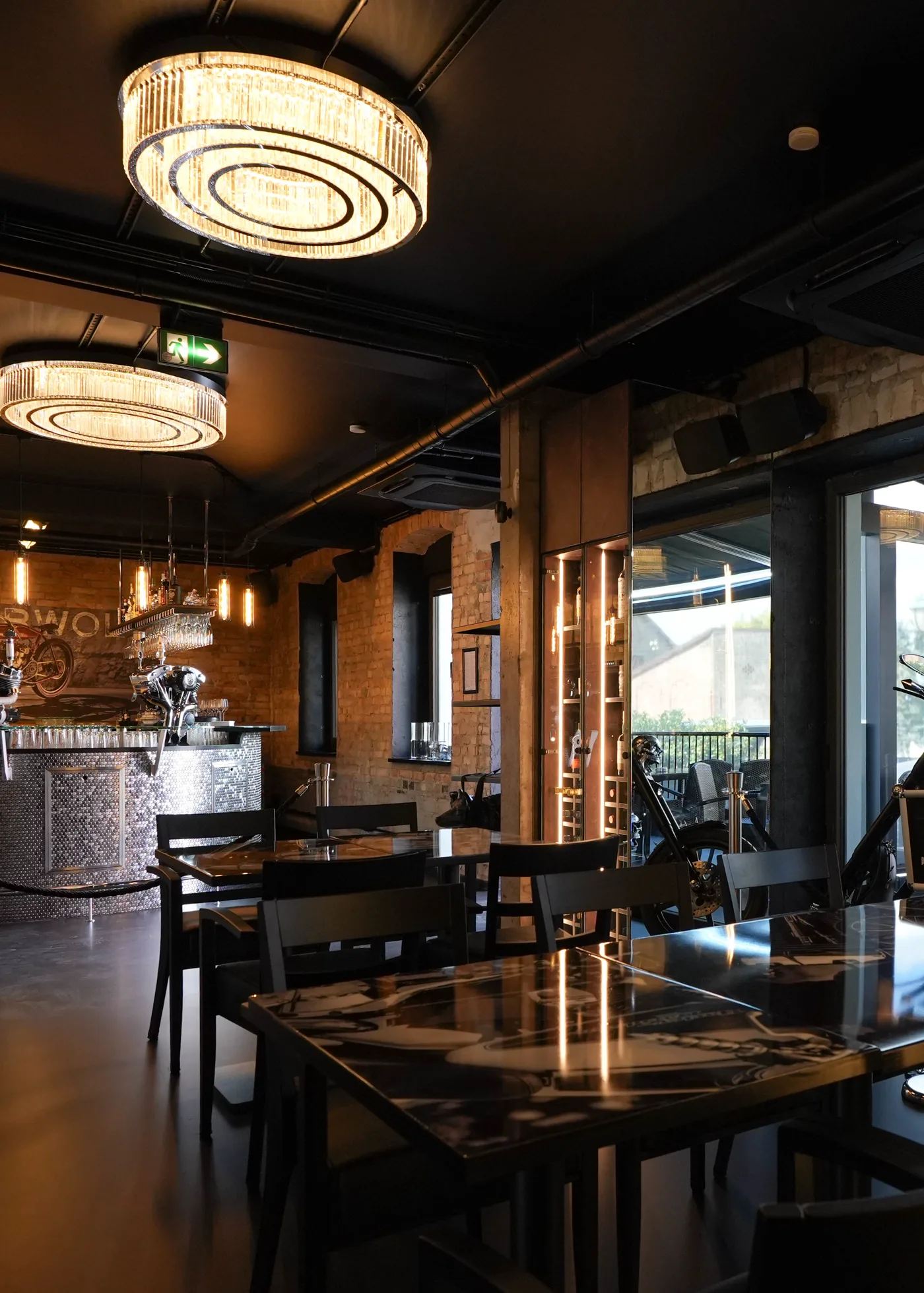 Blick durch das Restaurant zur runden Bar: gedeckte Tische, Kronleuchter und die offene Front zur Terrasse