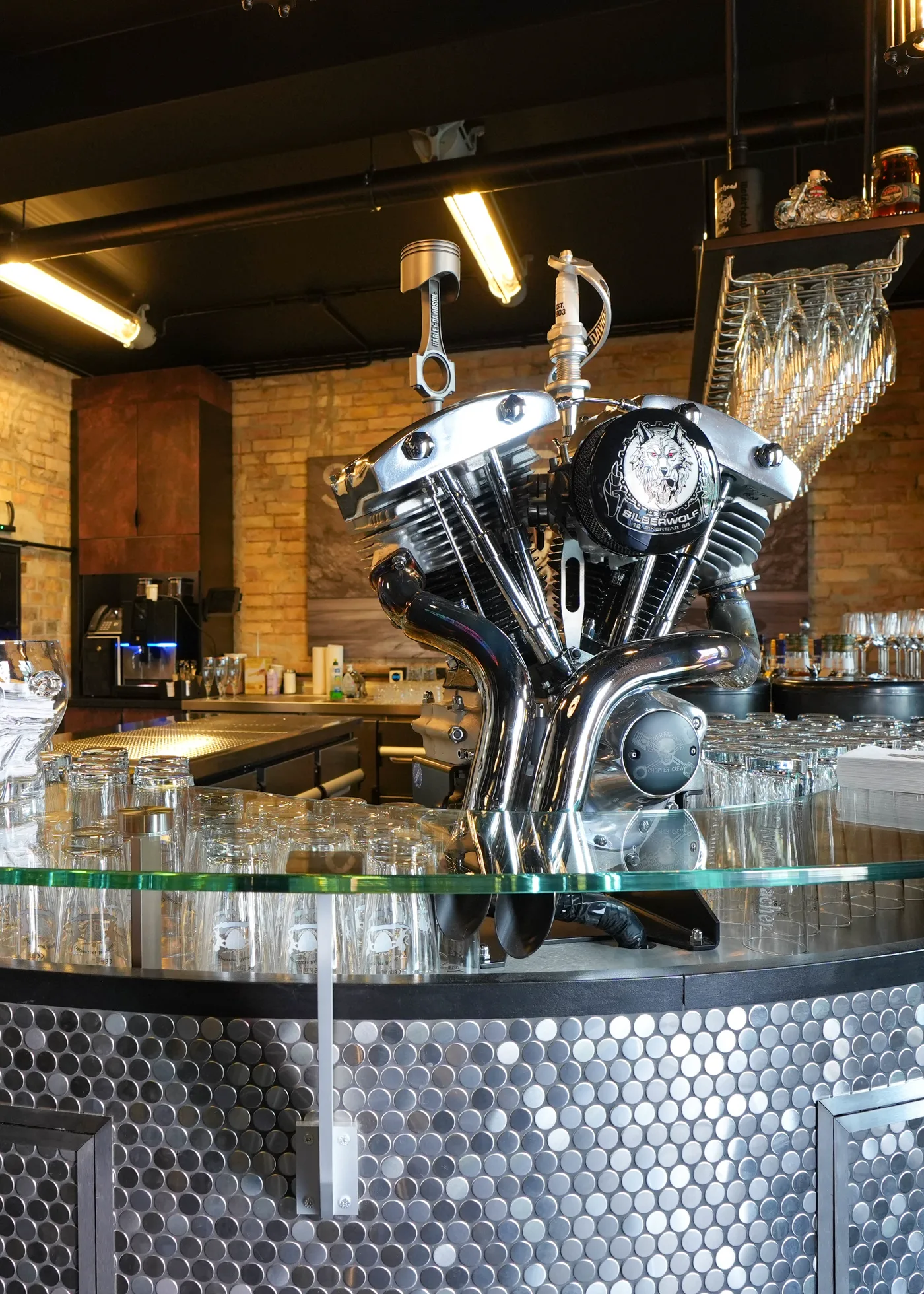 Der Tresen der Silberwolf Biker Bar: runde Theke mit genoppter Edelstahlverkleidung und Glasplatte, darauf der verchromte V-Twin mit Silberwolf-Wappen
