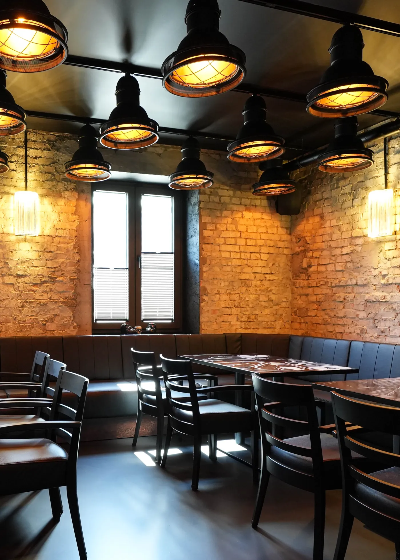 Dining room with a wrap-around leather bench, wooden tables, brick walls and a row of black industrial lamps