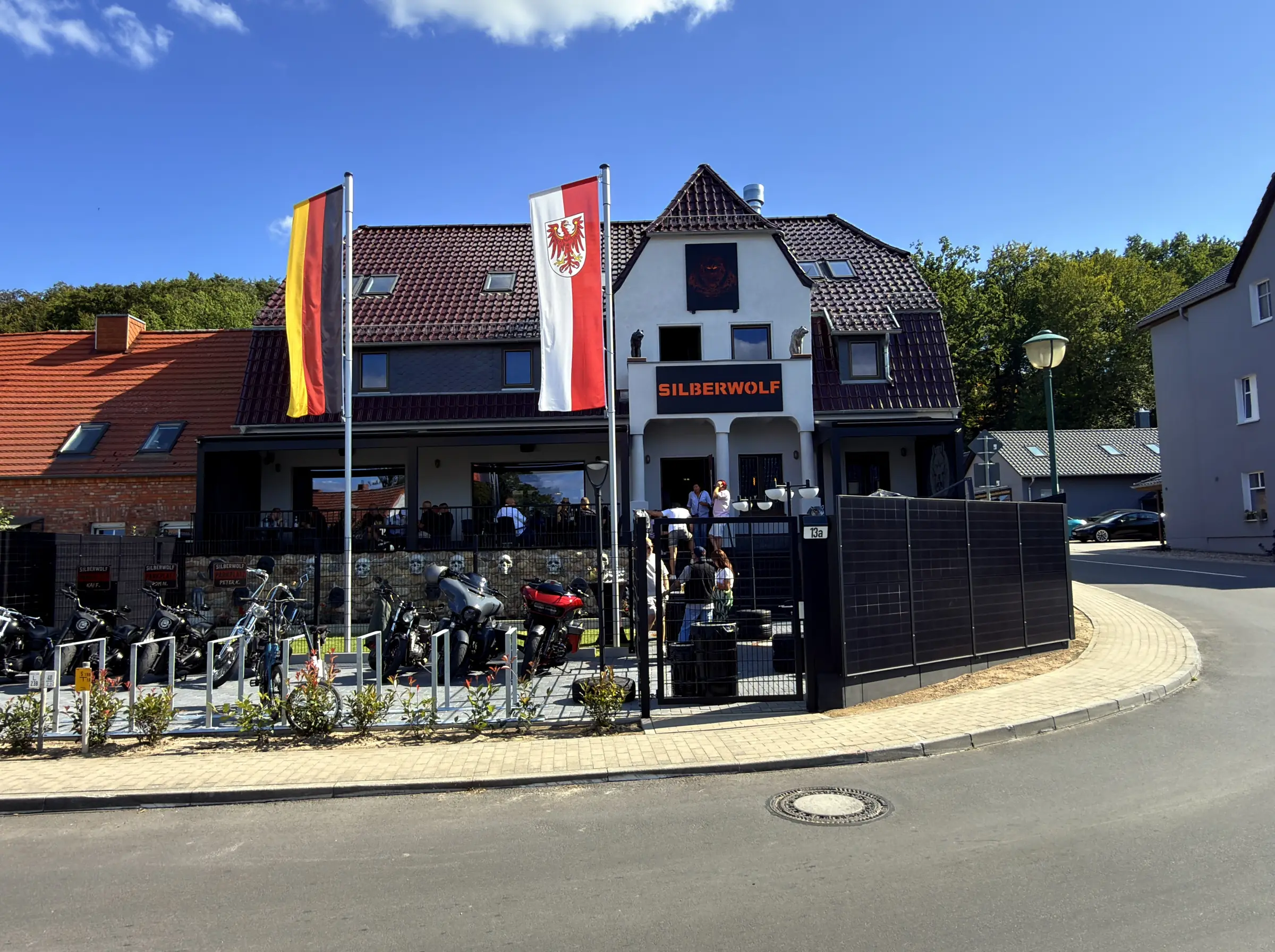 Exterior view of the Silberwolf Biker Bar: bright gable with the SILBERWOLF lettering, wolf figures beside the steps and skulls set into the fieldstone wall