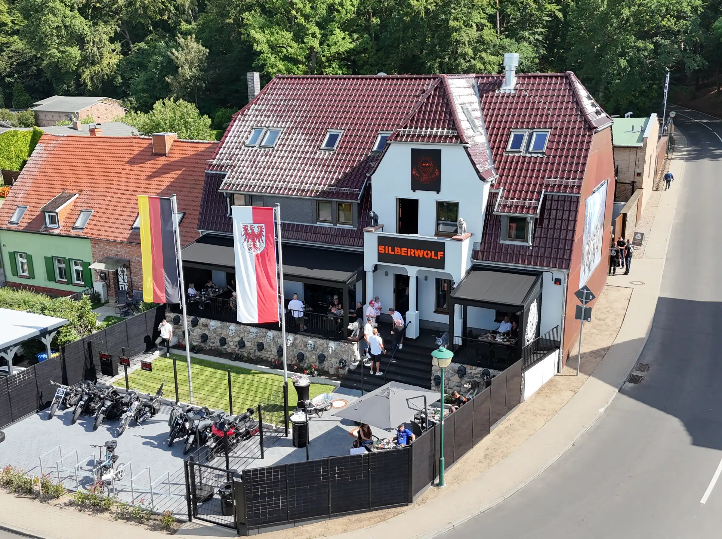 Luftaufnahme der Silberwolf Biker Bar: das Haus an der Straßenecke, davor der Hof mit abgestellten Motorrädern und die Terrasse