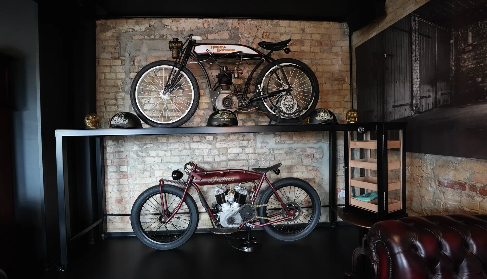 Harley-Davidson and Indian board-track racers mounted one above the other on the brick wall, golden skulls and helmets in front