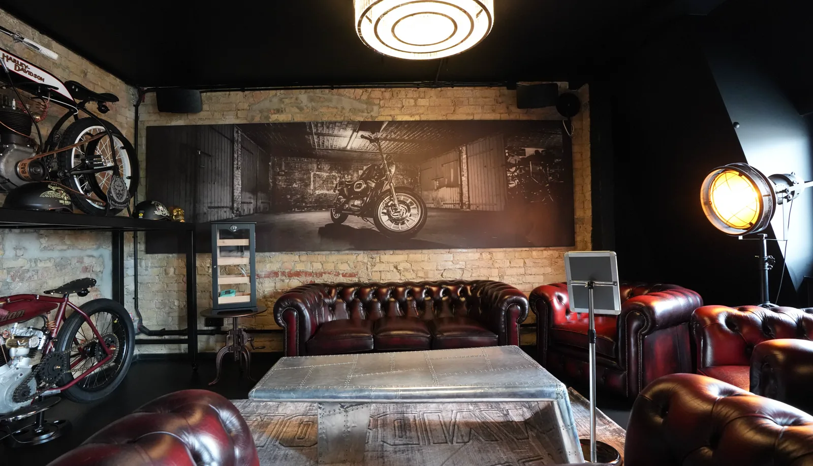 Chesterfield sofa beneath the large motorcycle mural, the humidor with cigars on the left, the studio lamp on the right