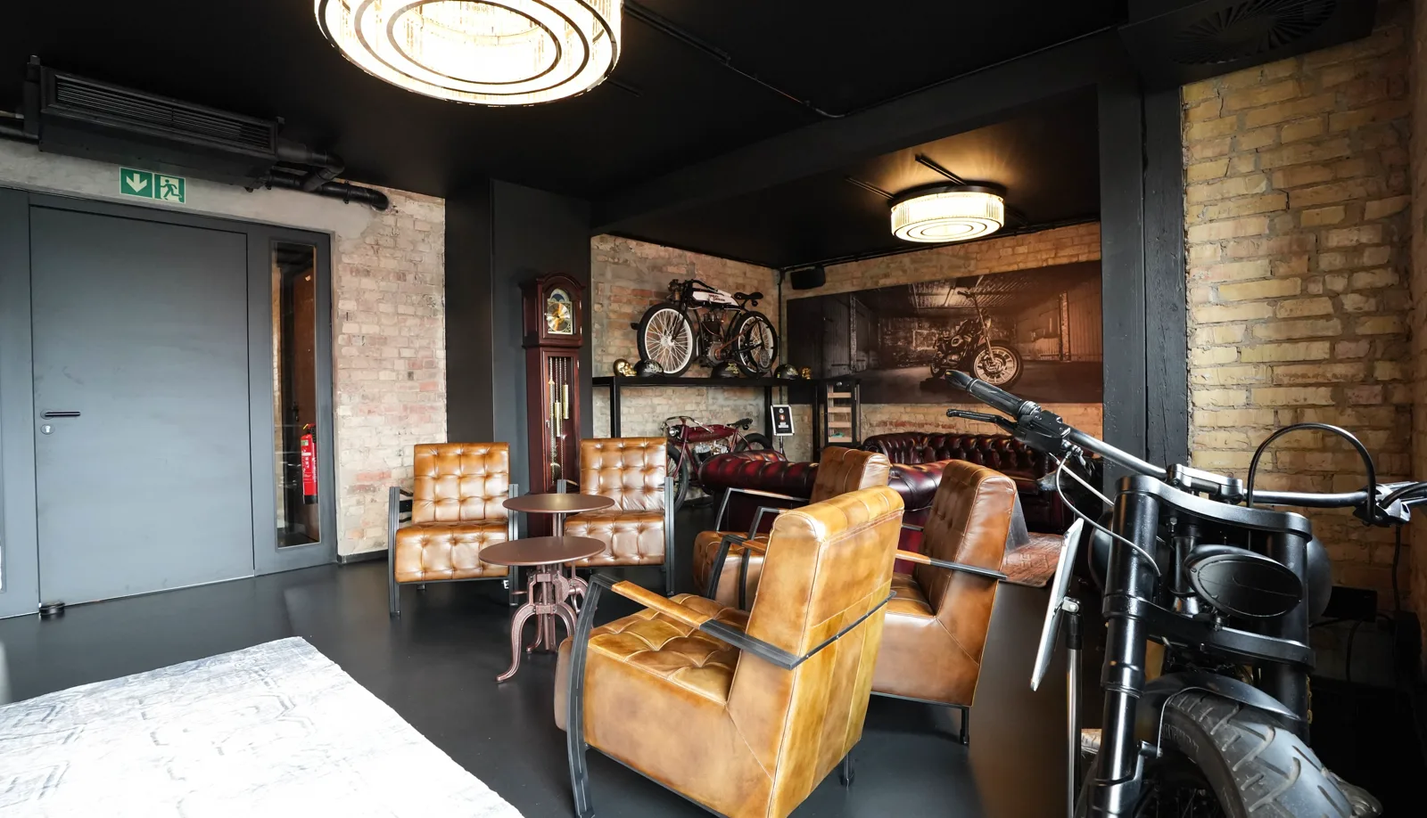 A look into the Herrenzimmer: leather chairs around two round tables, with grandfather clock, vintage motorcycles and Chesterfield sofas behind