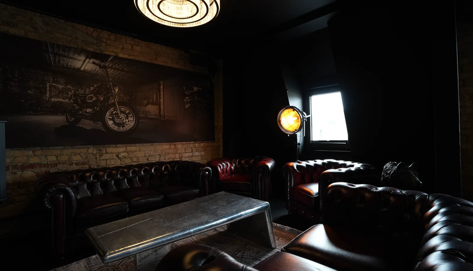 Chesterfield sofas beneath the large motorcycle mural in the Herrenzimmer, a studio lamp and the wolf's head beside them