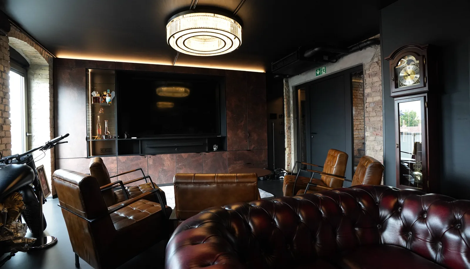 TV wall with illuminated whisky display in the Herrenzimmer, leather chairs and a Chesterfield sofa in front, the grandfather clock on the right