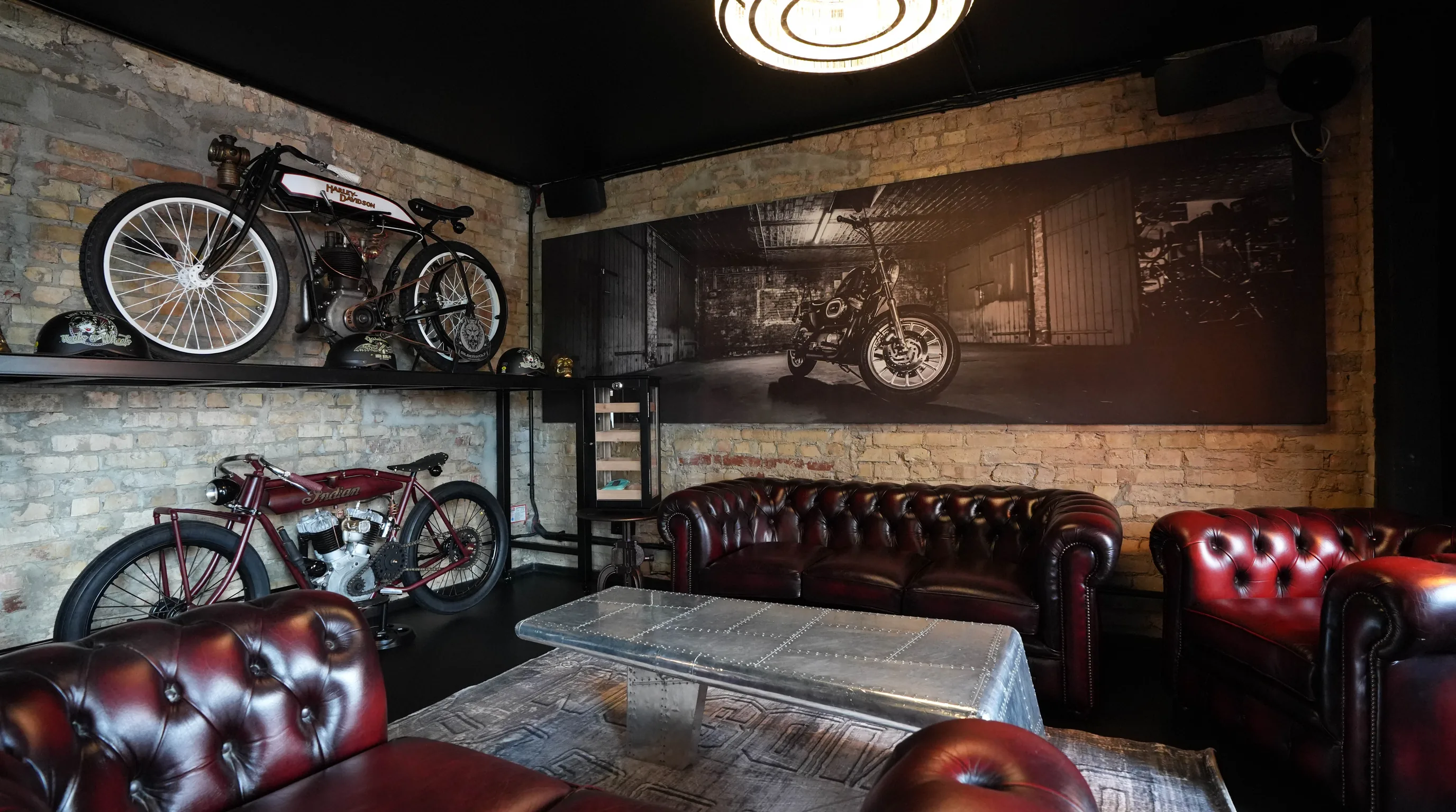Das Herrenzimmer der Silberwolf Biker Bar — Chesterfield-Ledersofas, großformatiges Motorrad-Wandbild und warmes Lampenlicht
