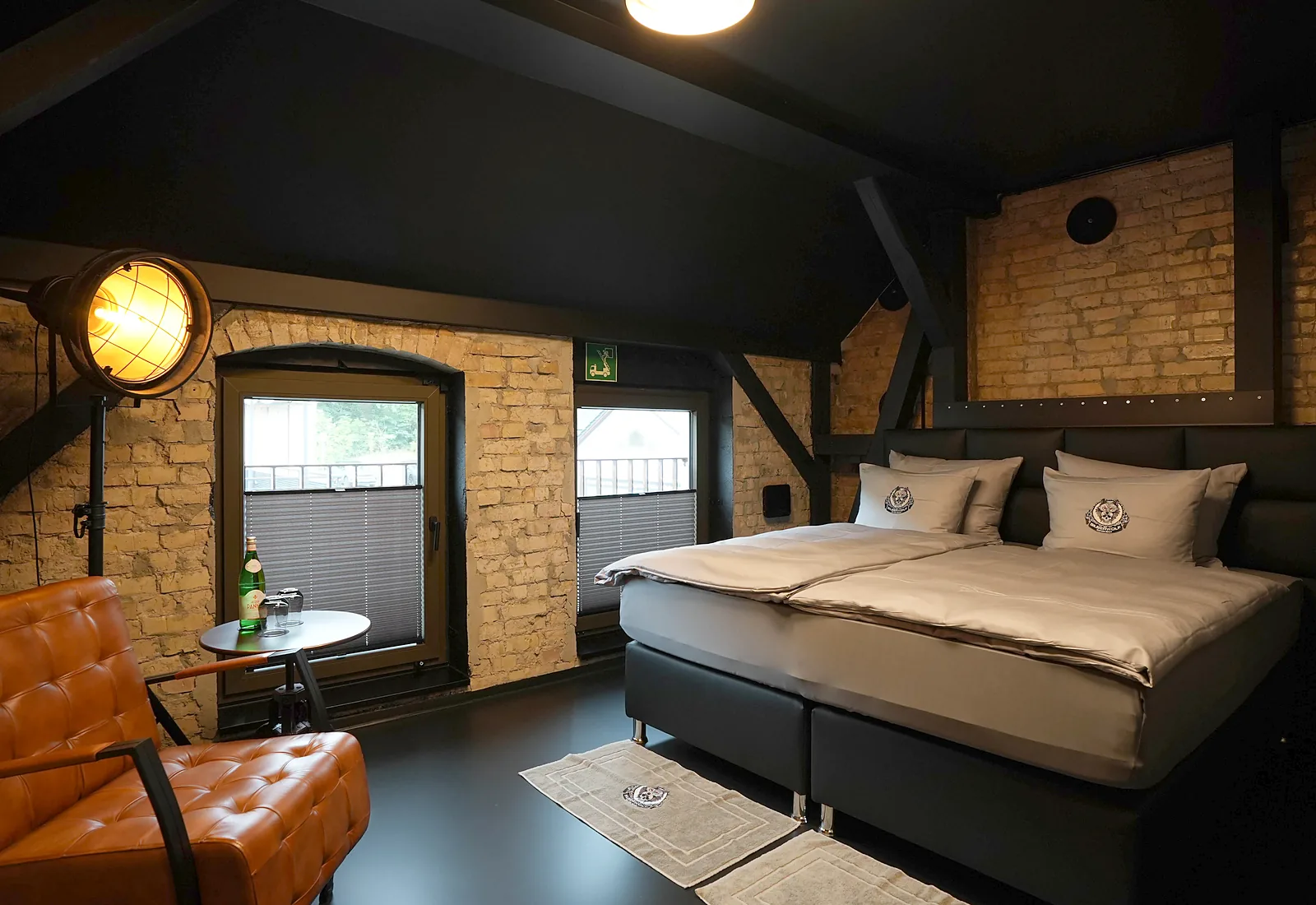 Fat Boy room: box spring bed against a brick wall, leather armchair and industrial floor lamp