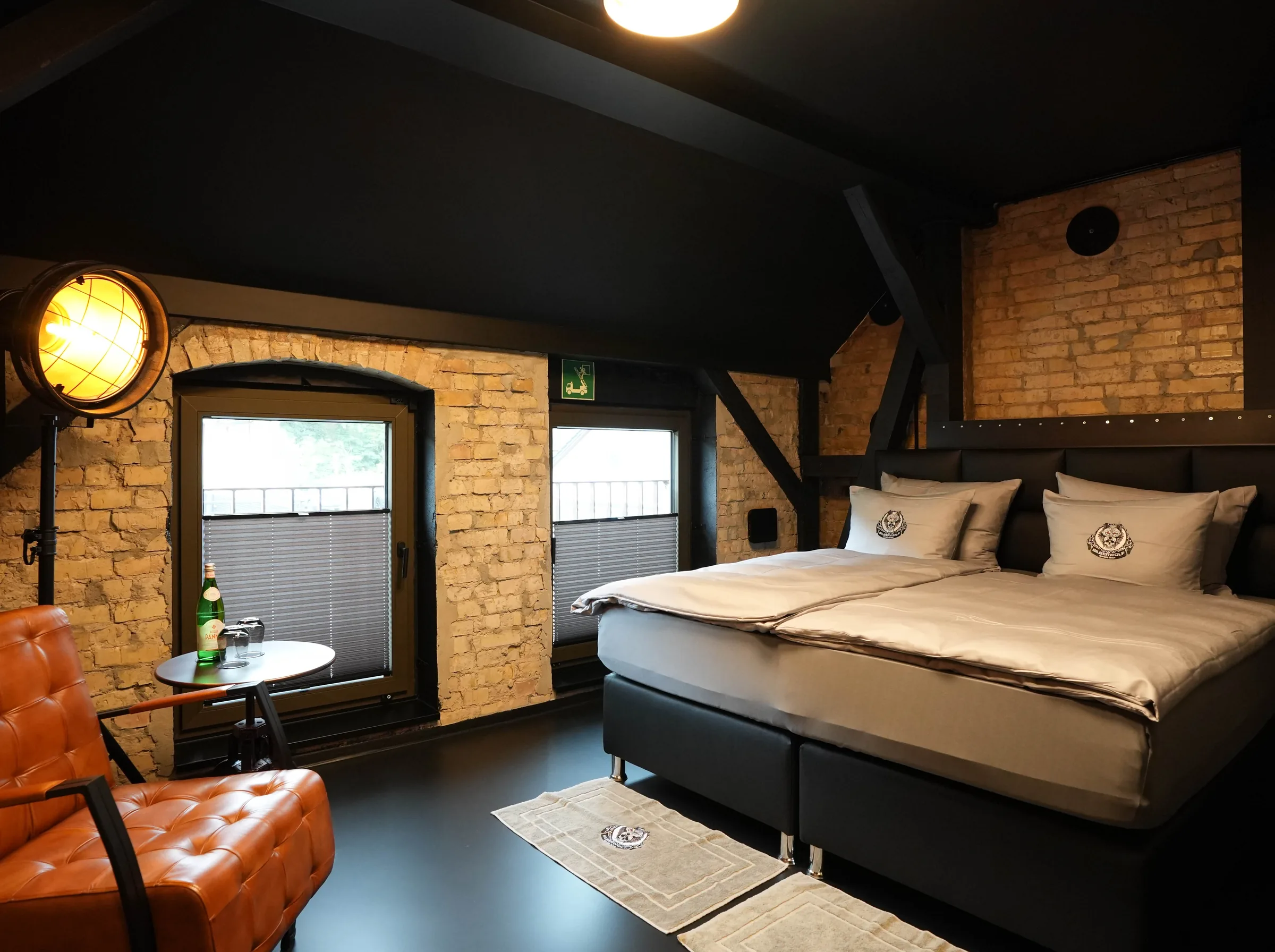 Fat Boy room — box-spring bed against a brick wall, leather chair and industrial floor lamp