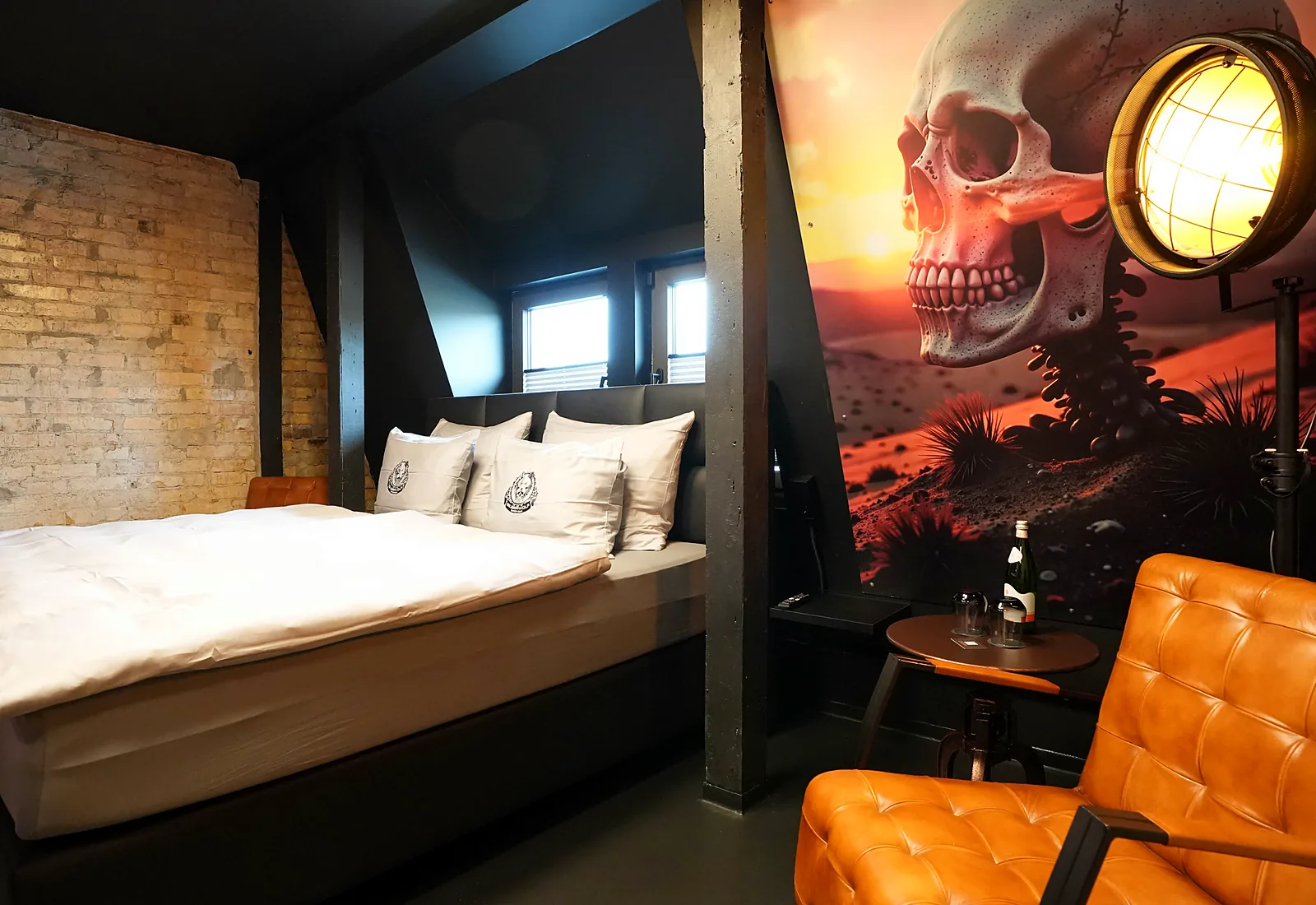 Ghostrider room: bed against a brick wall, next to it a large mural with a skull in the desert