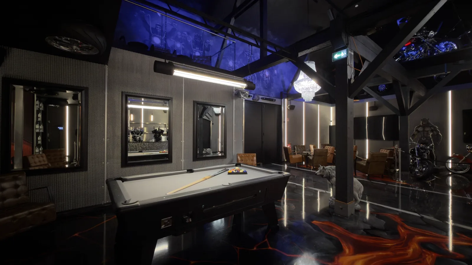 Pool table in the barn, behind it a werewolf figure and machines beneath the blue-lit ceiling
