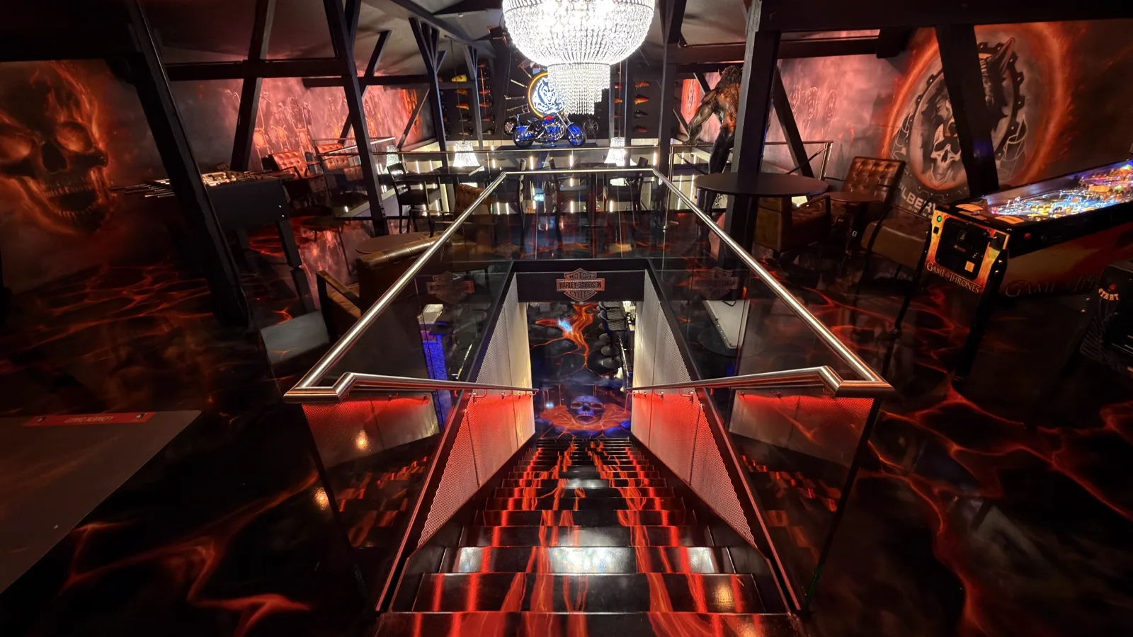 View from the gallery down the glass staircase into the barn, the chandelier above, the glowing lava floor underfoot