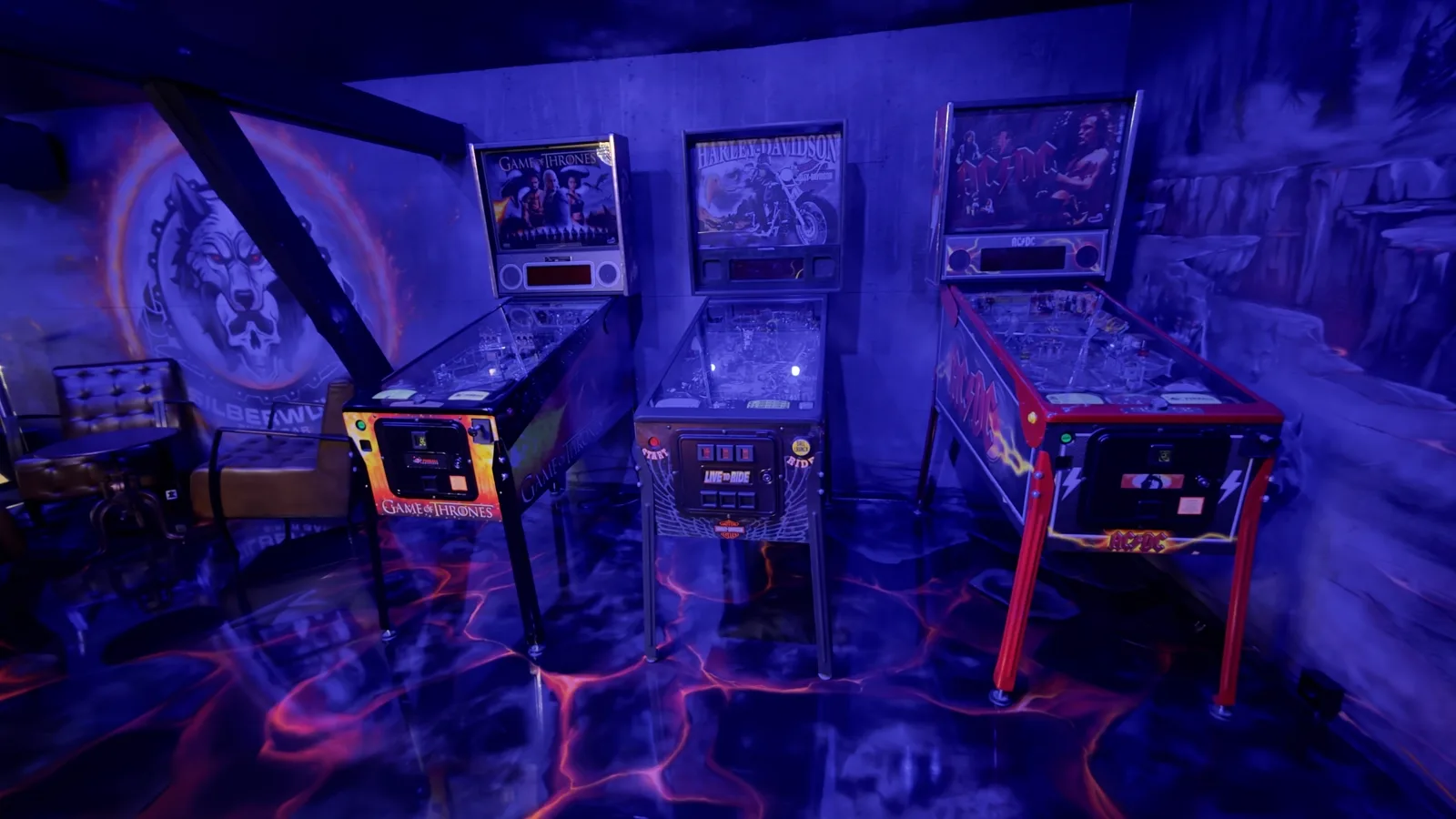 Three pinball machines in blue light on the barn's lava floor